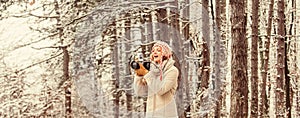 Stylish hipster traveler. woman holding photo camera. taking picture in winter forest. Photographer photographing on