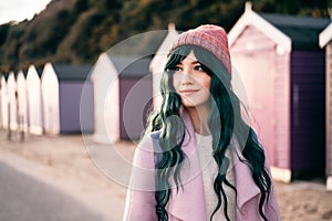 Stylish hipster woman with color hair in pink outfit and backpack walking along wooden beach huts on seaside. Off season