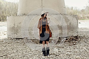 Stylish hipster woman in hat and fringe poncho and boots posing