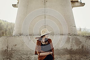 Stylish hipster woman in hat with windy hair posing near river s