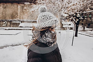 stylish hipster woman in knitted hat standing in snowy city street. beautiful fashionable girl in warm clothes in cold snow