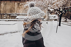 stylish hipster woman in knitted hat standing in snowy city street. beautiful fashionable girl in warm clothes in cold weather wi