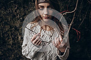 Stylish hipster woman posing in knitted sweater holding branch w