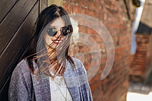 Stylish hipster woman smiling with windy hair at brick rustic wa