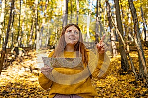 Stylish hipster woman traveler exploring map and showing path direction at autumn sunny forest