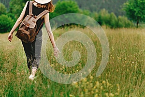 Stylish hipster woman walking in grass and holding in hand herb