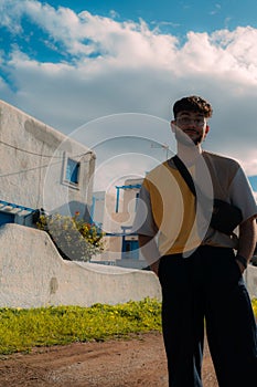 Stylish Hispanic man standing near a white modern building near a dirt road in a rural setting