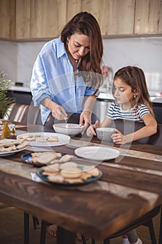 Mom and daughter prepare icing for gingerbread in their home kitchen. Beat with a blender. The girl helps the woman.