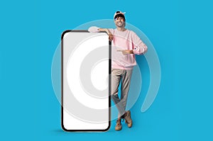 Stylish indian guy standing by huge smartphone with blank screen