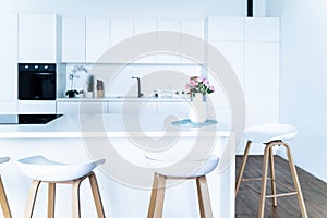 Stylish interior design of a modern fashionable snow-white kitchen in a minimalist style with an island and two bar stools, huge f