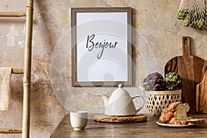 Stylish interior of kitchen space with wooden table, brown mock up photo frame, herbs, vegetables, tea pot, cups.