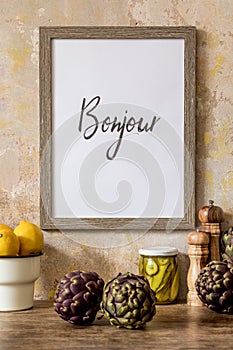 Stylish interior of kitchen space with wooden table, brown mock up photo frame, herbs, vegetables, tea pot, cups.