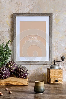 Stylish interior of kitchen space with wooden table, brown mock up photo frame, herbs, vegetables, tea pot, cups and kitchen.