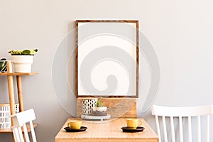 Stylish interior of kitchen space with wooden table with mock up photo frame, design chairs, decoration and furniture.