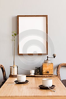 Stylish interior of kitchen space with wooden table with mock up photo frame, design chairs, decoration and furniture.