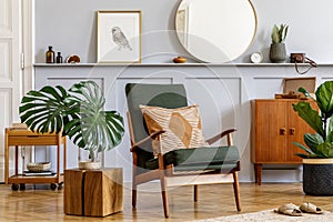 Stylish interior of living room with design armchair, wooden vintage commode, round mirror, shelf, tropical leaf, coffee table.