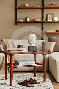 Stylish interior of living room with design wooden coffee table, beige sofa, cup of coffee, book, decoration.