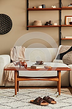 Stylish interior of living room with design wooden coffee table, beige sofa, cup of coffee, book, decoration.