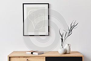 Stylish interior of living room with mock up poster frame, wooden commode, book, leaf in ceramic vase.