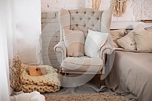 The stylish interior of the room with comfortable grey armchair and pillows. Cozy decorated living room for Christmas. Rustic home