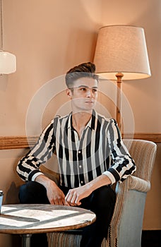 Stylish Italian in a cafe. Male model sitting on a chair in a restaurant. Handsome guy in the interior with a lamp by