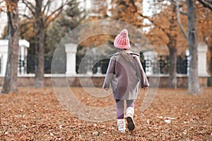 Stylish kid girl 4-5 year old wear knit hat, jacket walk in park over nature background.