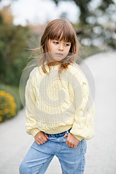 Stylish kid girl 5-6 year old wear trendy casual sweater and jeans pants walking in park outdoors.