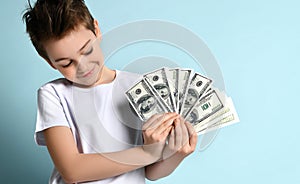 Stylish kid looking on fan of dollar banknotes in his hands with admire imagining how much he can purchase.