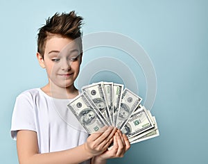Stylish kid looking on fan of dollar banknotes in his hands with admire imagining how much he can purchase.