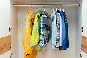 Stylish kids clothes in white wardrobe closet. Kids clothing on hangers in the closet. Storage organization