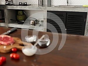 Stylish kitchen, on a wooden table there is a piece of fresh meat with spices, tomatoes and herbs, minimalist interior