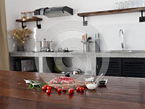 Stylish kitchen, on a wooden table there is a piece of fresh meat with spices, tomatoes and herbs, minimalist interior