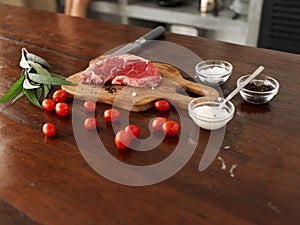 Stylish kitchen, on a wooden table there is a piece of fresh meat with spices, tomatoes and herbs, minimalist interior