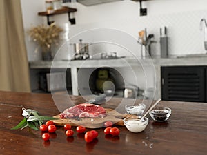 Stylish kitchen, on a wooden table there is a piece of fresh meat with spices, tomatoes and herbs, minimalist interior