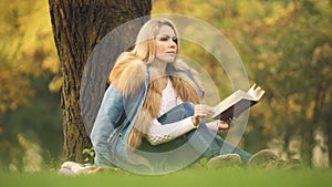 Stylish lady reading adventure book in central park, sitting under tree, autumn