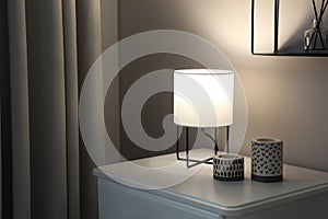 Stylish lamp and candles on white nightstand in room, space for text