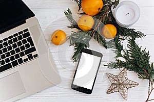 stylish laptop and phone with empty screen on white wooden background with christmas oranges and golden star and candle. flat lay