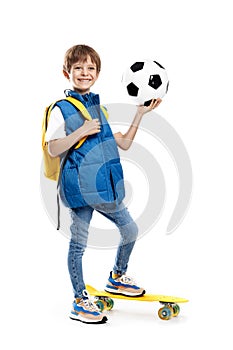 Stylish little boy with skateboard and backpack holding soccer ball on white background. Back to School.