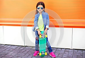 Stylish little girl child with skateboard wearing a sunglasses and checkered shirt