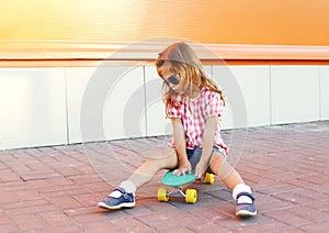 Stylish little girl child with skateboard wearing sunglasses in city