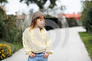 Stylish little kid girl 4-5 year old wear casual yellow knit woolen sweater and denim pants walk in park outdoors over nature back