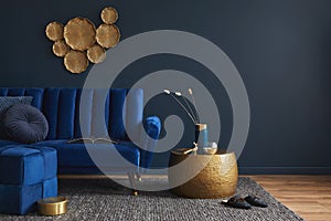 Stylish living room interior composition with velvet blue sofa, golden side table, pouf, pillows and elegant home decor.