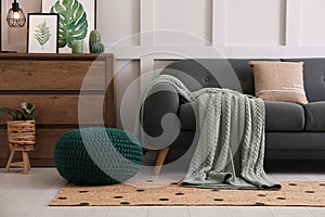 Stylish living room interior with knitted pouf, sofa and wooden chest of drawers