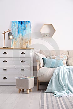 Stylish living room interior with ottoman, sofa and white wooden chest of drawers