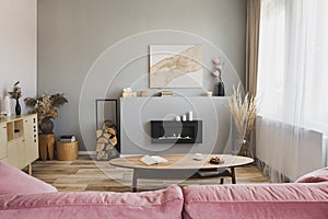 Stylish living room interior with pastel pink sofa, wooden coffee table and eco fireplace