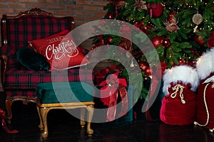 Stylish loft interior of room with Christmas fir tree and checkered armchair. Red sack santa claus with gifts near big Christmas f