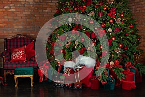 Stylish loft interior of room with Christmas fir tree and checkered armchair. Red sack santa claus with gifts near big Christmas f