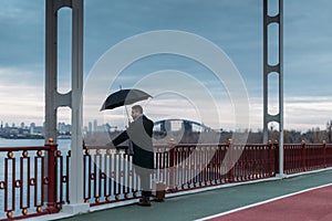 stylish lonely man with umbrella and suitcase standing