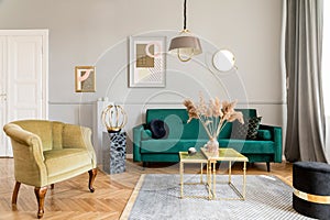 Stylish and luxury living room interior with elegant green velvet armchair, sofa, mock up poster and decoration.