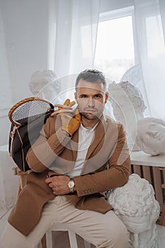 Stylish male embodies the old-money look, posing with a bag and tennis racket